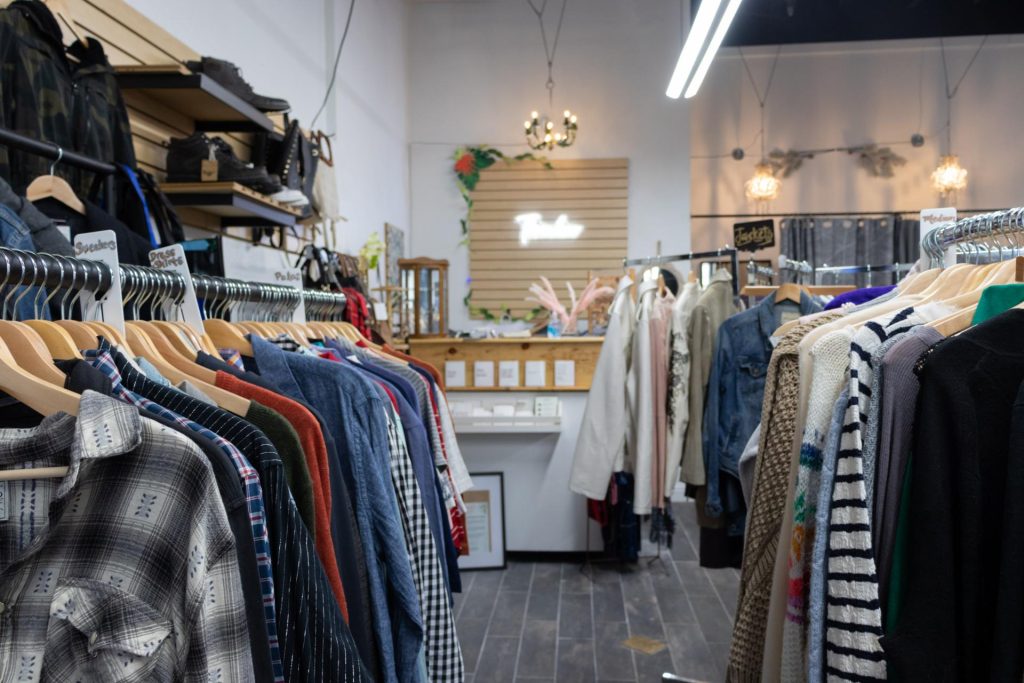 Cozy boutique with rows of colorful shirts and jackets on wooden hangers, soft lighting, rustic decor, and a welcoming, stylish atmosphere.