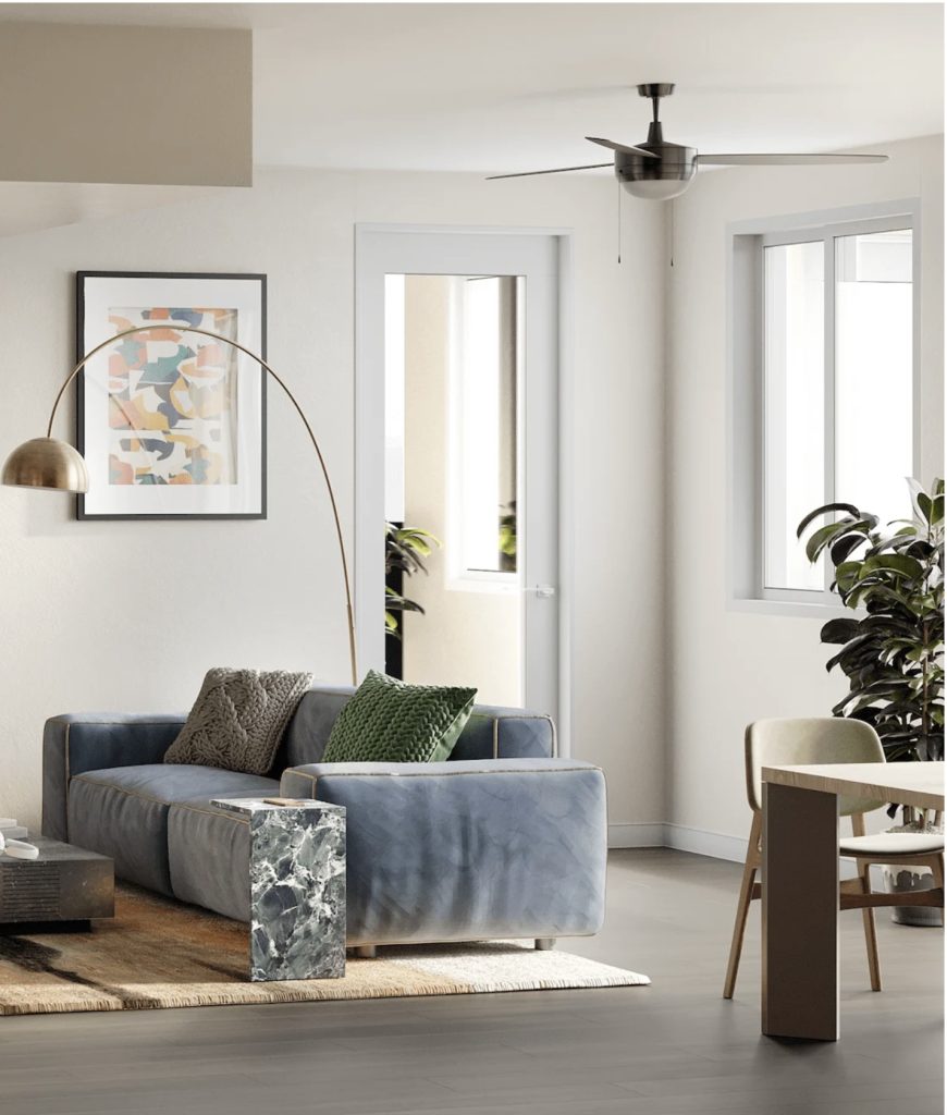 Modern living room with a blue sofa, green and gray cushions, arc lamp, abstract wall art, ceiling fan, and indoor plants. Bright and cozy ambiance.