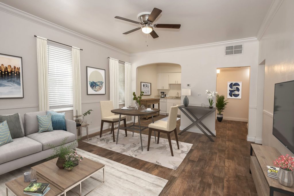 Spacious living room with a modern design featuring a gray couch, wooden floor, round dining table, potted plants, vibrant artwork, and ceiling fan. Cozy and inviting ambiance.
