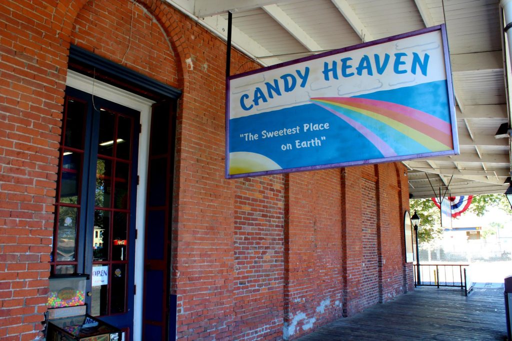 Brick building with a colorful "Candy Heaven" sign featuring a rainbow and the motto "The Sweetest Place on Earth," evoking a cheerful, inviting atmosphere.