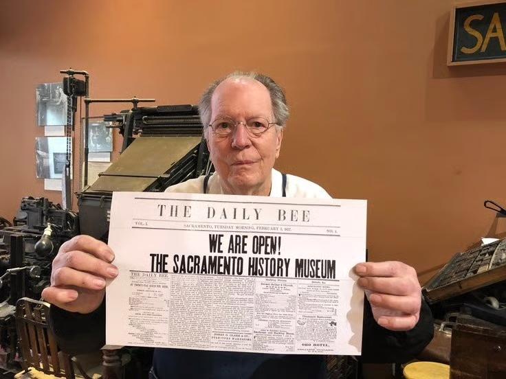 Older man in Sacramento History Museum, holding a copy of The Daily Bee where the headline reads, "We are Open! The Sacramento History Museum."