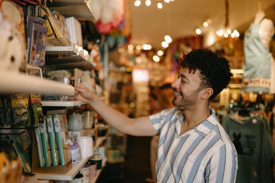 A man in a striped shirt smiles while browsing a colorful, well-lit store filled with various items. The atmosphere is warm and inviting.