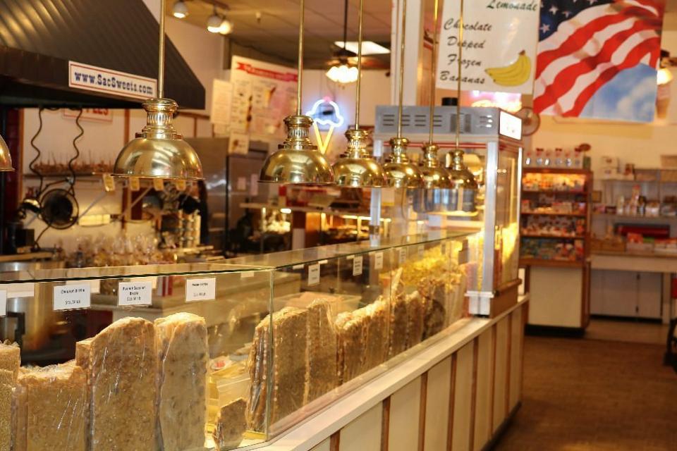 A cozy candy shop with a glass counter displaying various nougats. Brass lamps hang above, and an American flag decorates the warm, inviting space.